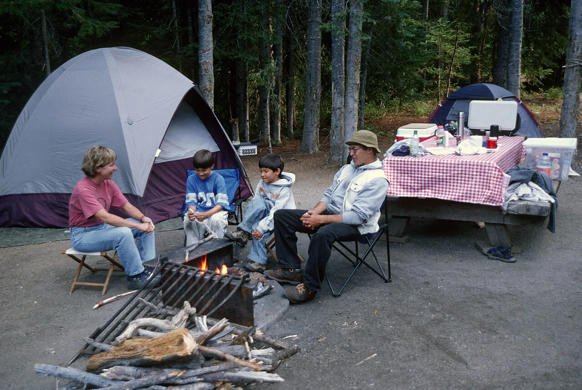 Family tent pitched at a wooded campground with kids playing nearby — 2
